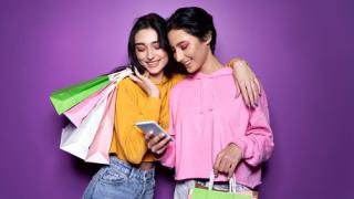 Two girls with shopping bags looking at a smartphone