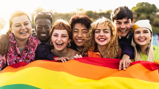 A diverse group of people holding a rainbow flag
