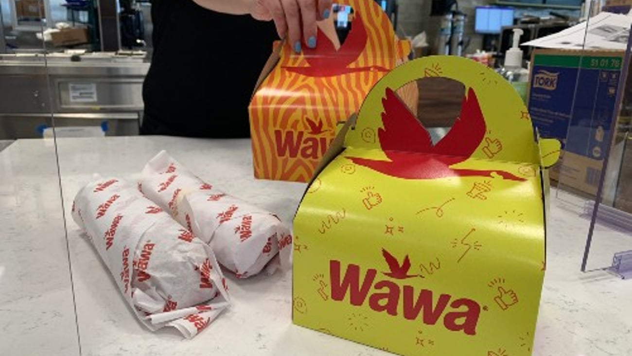 A Wawa associate sets out two Kids Meals and and two hoagies on a counter