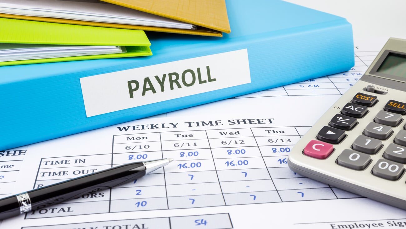 PAYROLL word on blue binder placed on weekly time sheet for overtime