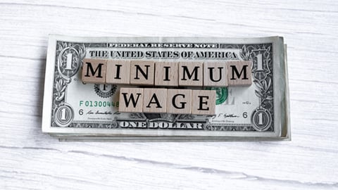 A dollar bill with minimum wage in scrabble tiles