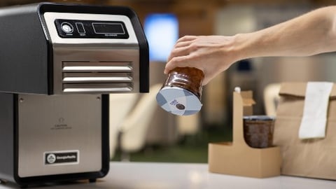 GP Pro Automated Sealing Machine for beverages, along with a hand holding a sealed cup upside down 