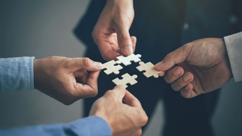 Four people holding pieces of a jigsaw puzzle