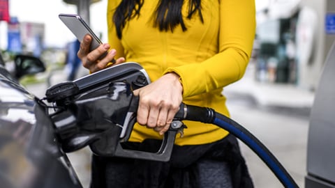 A women fills up her gas tank while checking her cell phone