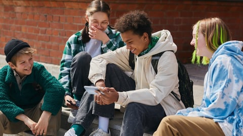 Group of friends sitting on steps of building outdoors and laughing while watching funny video on mobile phone; Shutterstock ID 2169268281