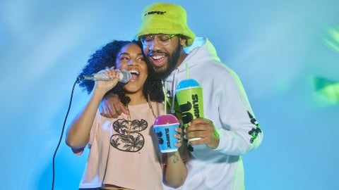 A man and a woman hold Slurpees while singing into a microphone