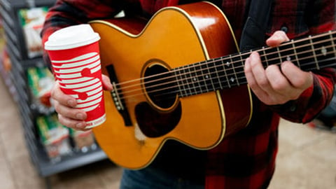 A guy playing a guitar and holding a Speedway coffee