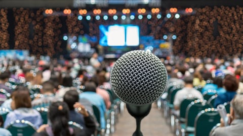 People seating in a large conference room with a microphone