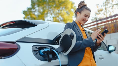 Girl reads her phone while her electric car charges