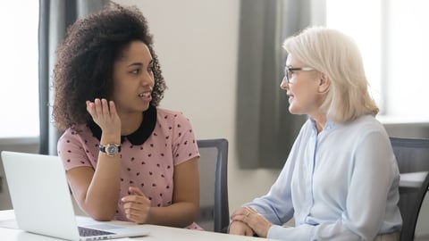 Diverse old and young female colleagues talking at work, african and caucasian business women sitting together in office having friendly conversation, mentor intern discussing planning shared project; Shutterstock ID 1332825527