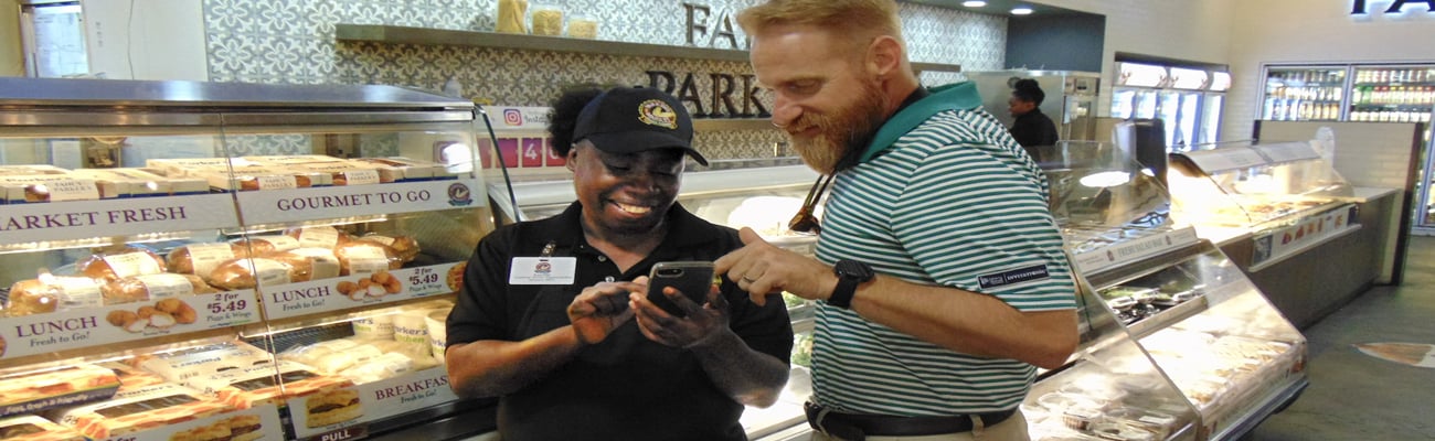 Parker’s Chief Human Resources Officer Corey McClimans shows Lucille Washington, deli associate, how to use the new DailyPay technology.