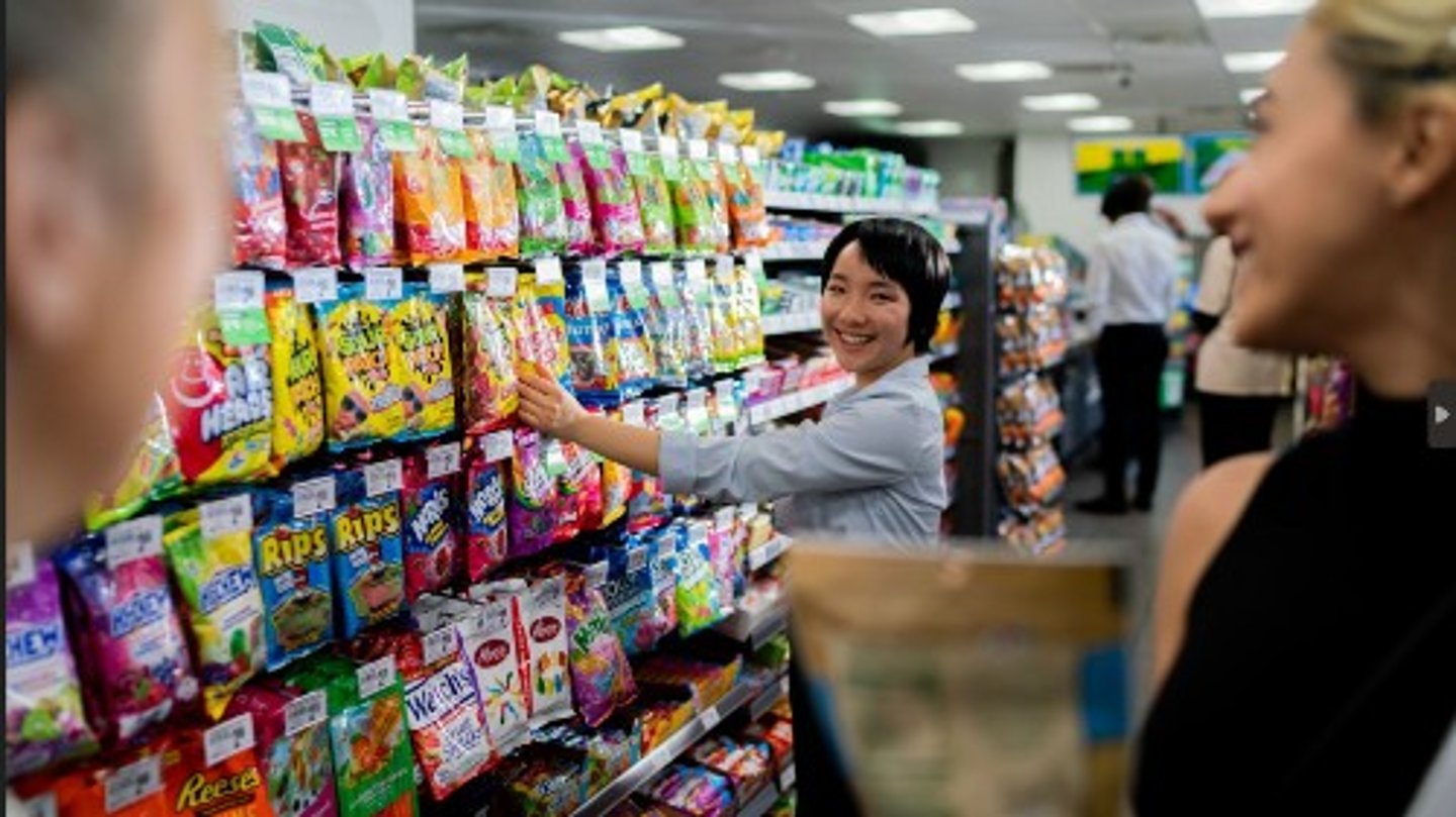 7-Eleven clerk in snack aisle talking to customers