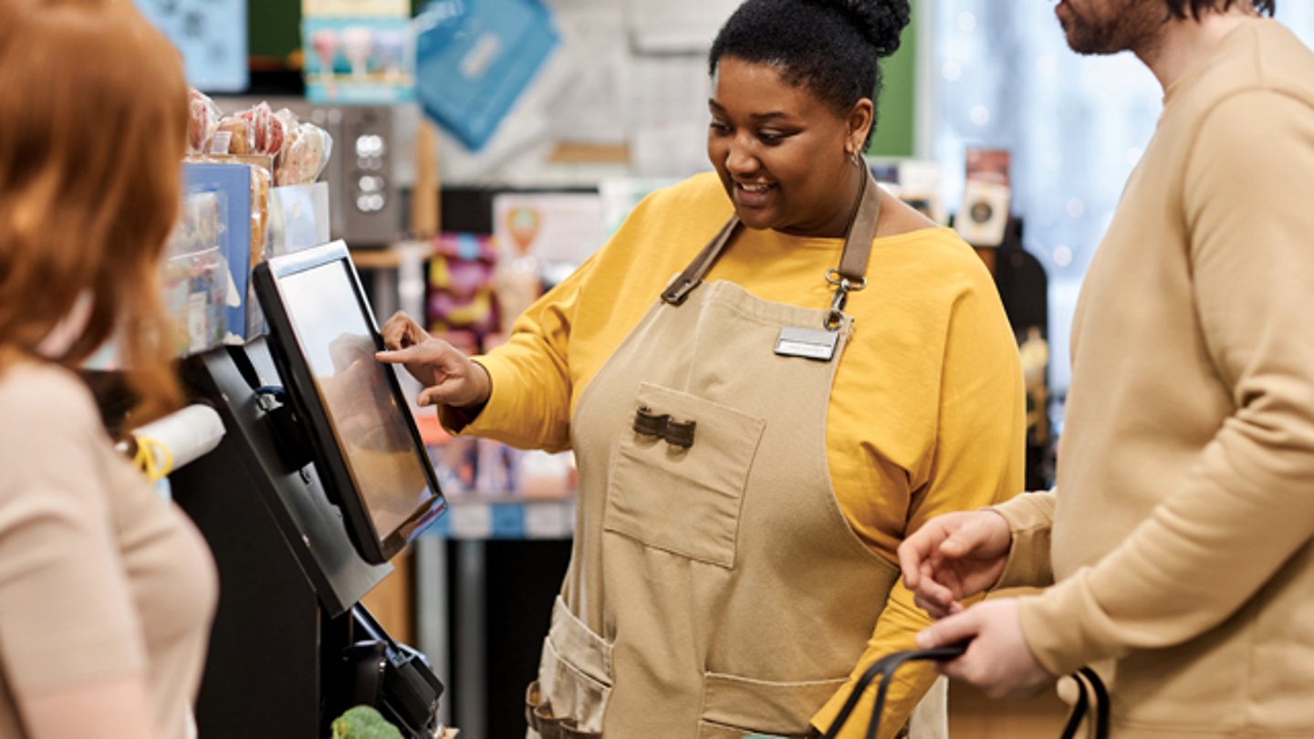 A store employee showing two customers how to use a touchscreen kiosk