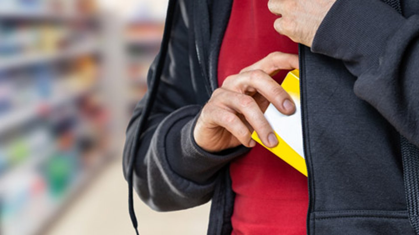 A man stealing something from a store and putting it in his jacket pocket