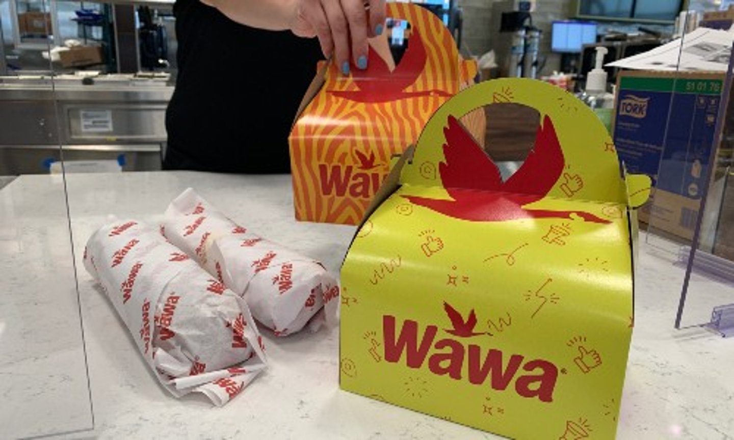 A Wawa associate sets out two Kids Meals and and two hoagies on a counter