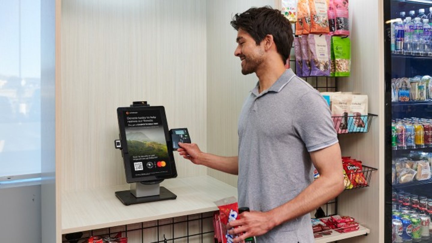 Man using a Cantaloupe touchscreen with Mastercard advertising