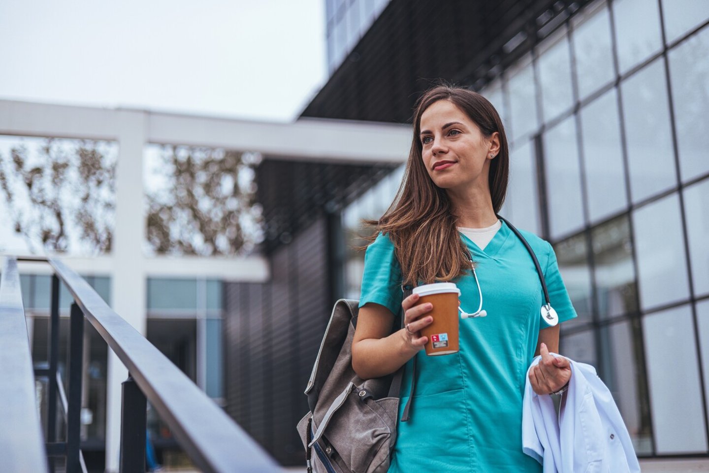 A female doctor holding a cup of coffee outside a hospital