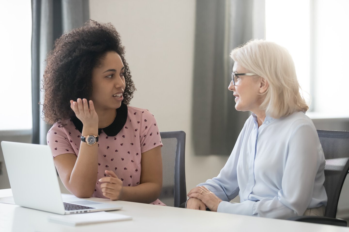 Diverse old and young female colleagues talking at work, african and caucasian business women sitting together in office having friendly conversation, mentor intern discussing planning shared project; Shutterstock ID 1332825527